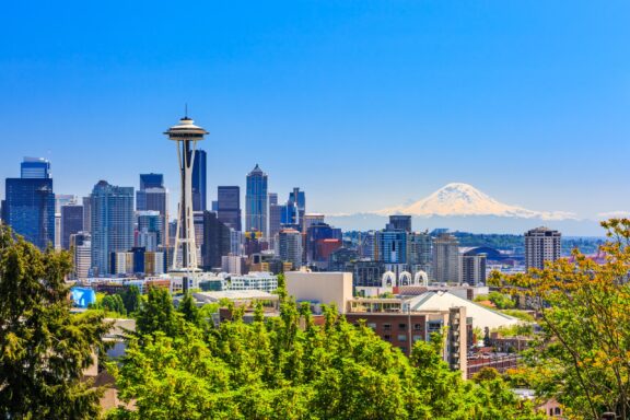 Panoramic view of the Seattle skyline with the Space Needle on the left and Mount Rainier in the background on a clear, sunny day.