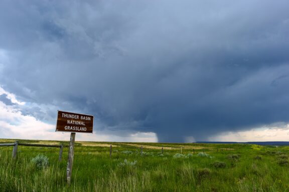 A landscape depicting Thunder Basin National Grassland under dark, stormy skies, with a sign indicating the name of the location on the left.